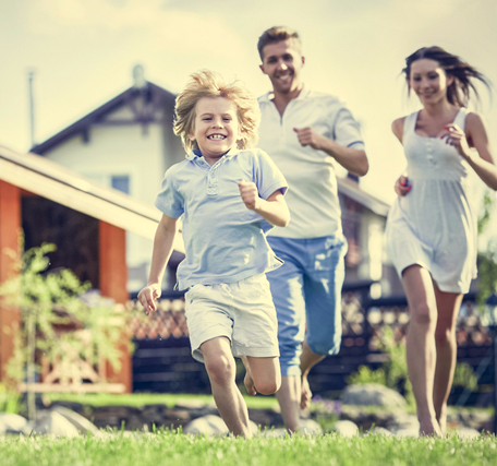 Photo of a happy mother, father, and child running together on a lawn with their house in the background
